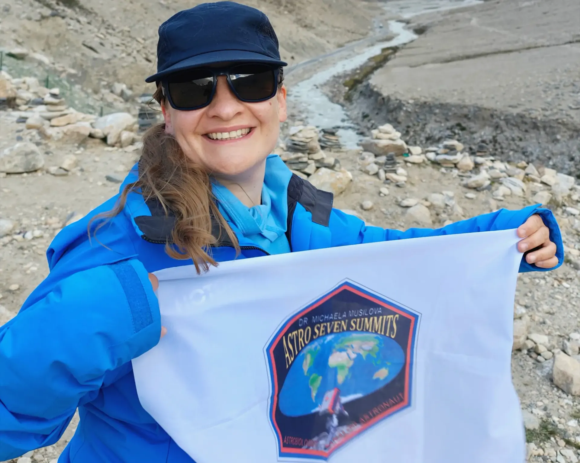 Dr. Michaela Musilova on her Astro Seven Summits mission. She is holding Astro Seven Summits flag in her hands, she is smiling.